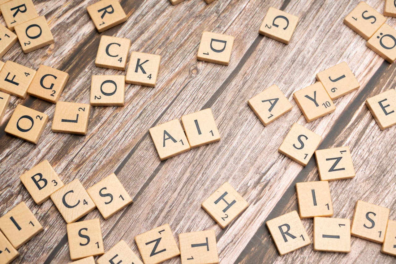 who-we-are Wooden letter tiles scattered on a textured surface, spelling 'AI'.