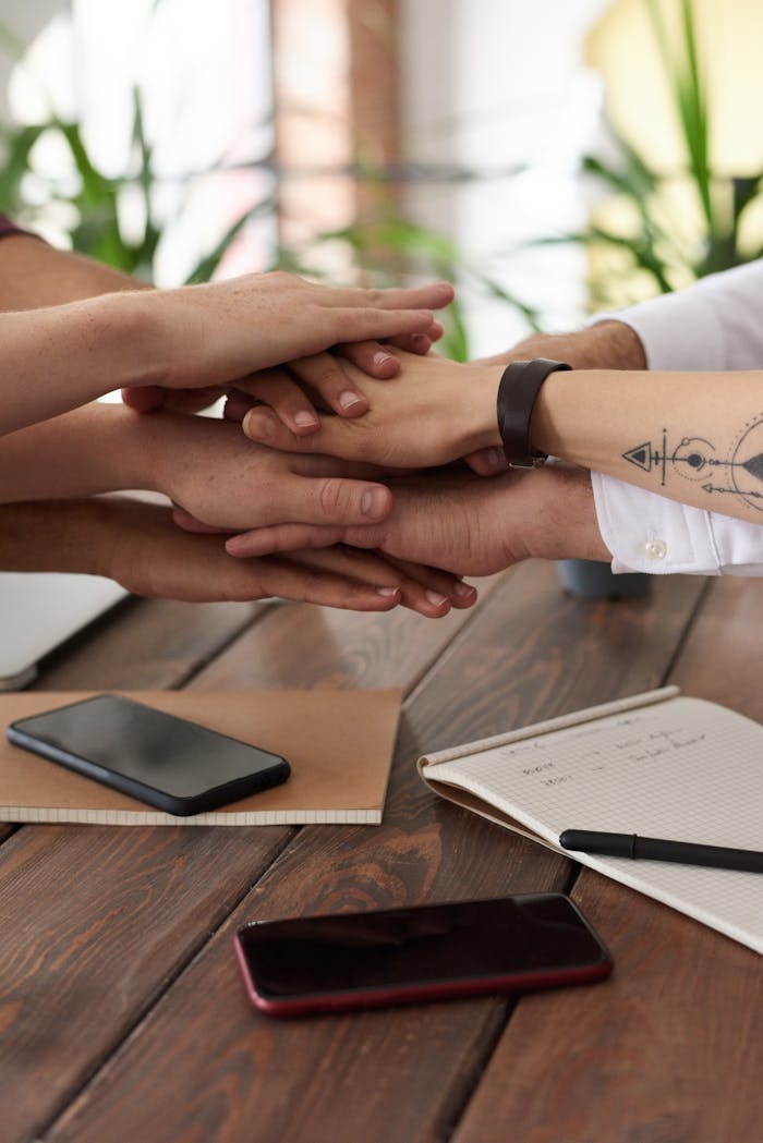 services-01 Hands from a diverse team stack on a table symbolizing unity and teamwork in a modern office setting.